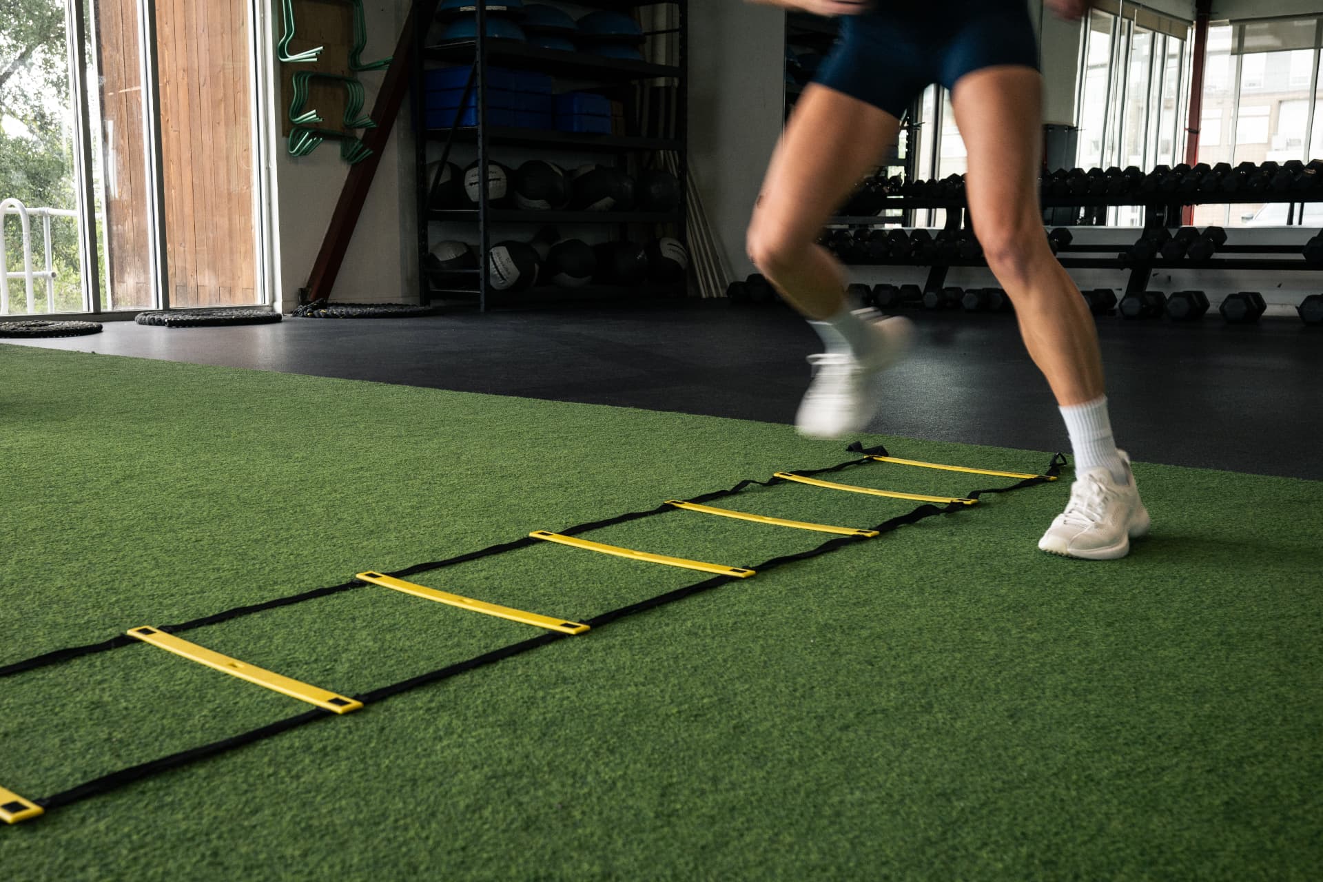 Member running an agility ladder drill on the turf at Athletic Outcomes Mueller